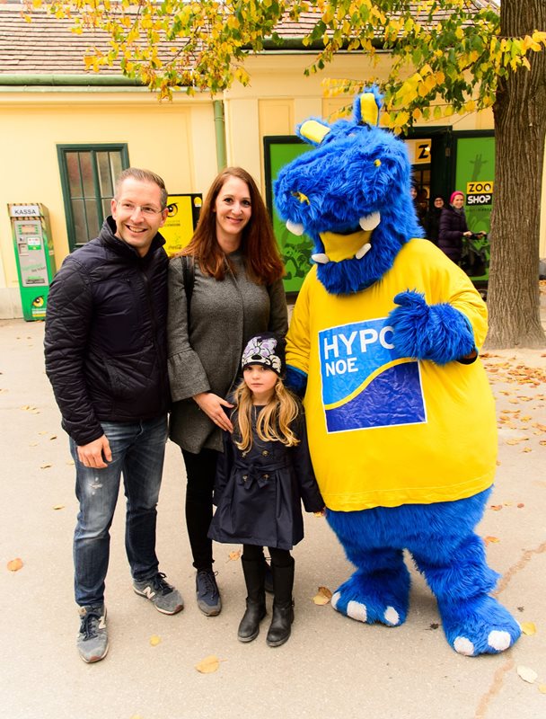 Das Maskottchen Hippo begrüßt eine Familie mit Kind im Tiergarten Schönbrunn.