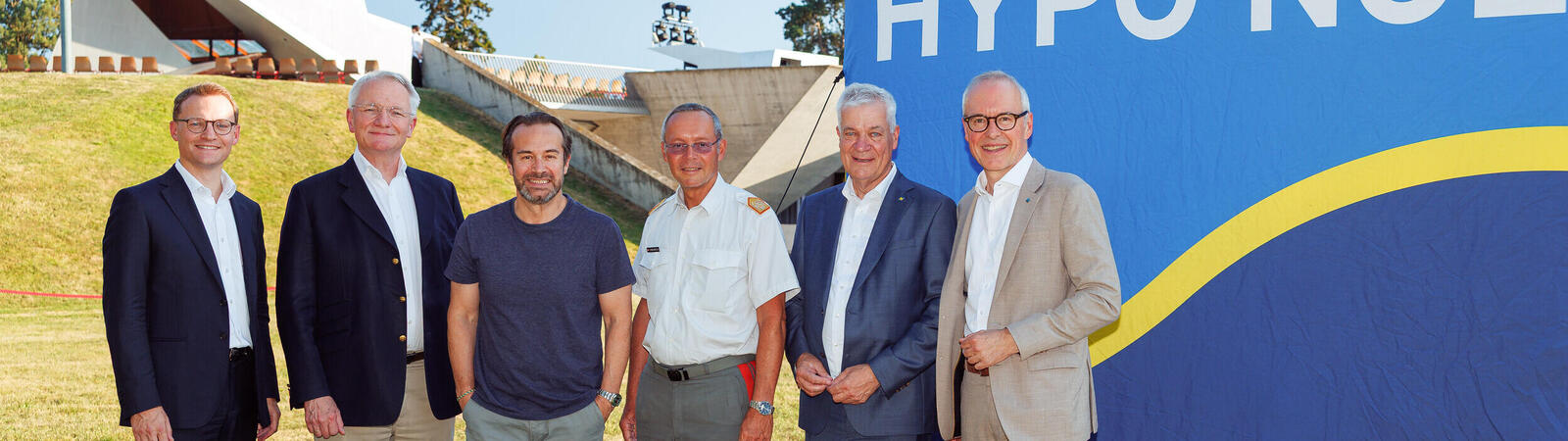 sechs Männer in Anzug stehen vor einem blauen Würfel mit Schriftzug "HYPO NOE" auf einer Wiese