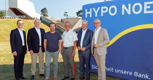 sechs Männer in Anzug stehen vor einem blauen Würfel mit Schriftzug "HYPO NOE" auf einer Wiese