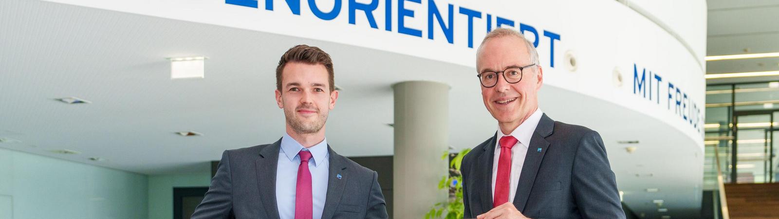 Zwei Männer in Anzug und Krawatte halten ein Schild mit gelben Hintergrund und blauer Aufschrift "HYPO NOE".