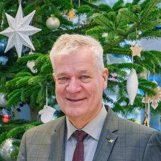 HYPO NOE Weihnachtsaktion Zwei Männer in Anzug stehen vor einem geschmückten Christbaum und halten je ein Geschenkspackerl in der Hand.