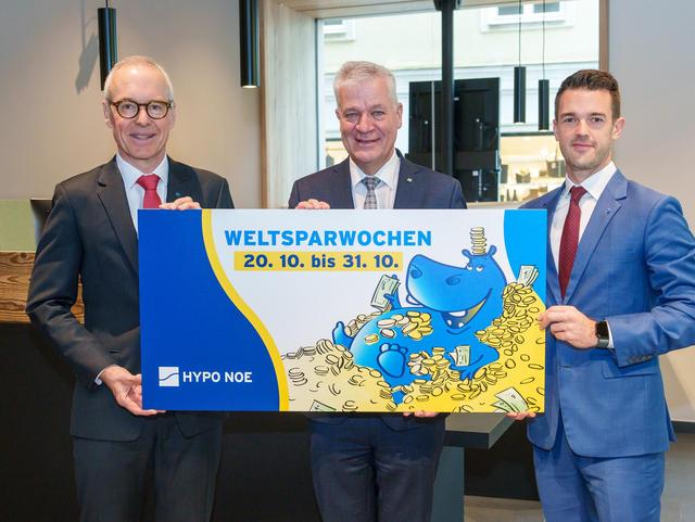 Drei Männer in Anzug und Krawatte halten ein Schild mit einem aufgedruckten Hippo und der Aufschrift "HYPO NOE Weltsparwochen von 20.10 bis 31.10.".