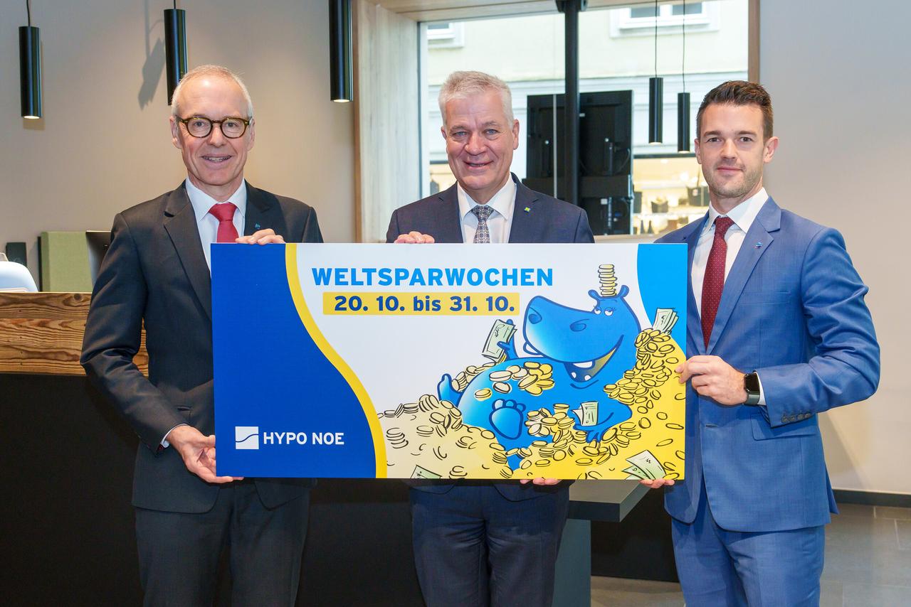 Drei Männer in Anzug und Krawatte halten ein Schild mit einem aufgedruckten Hippo und der Aufschrift "HYPO NOE Weltsparwochen von 20.10 bis 31.10.".
