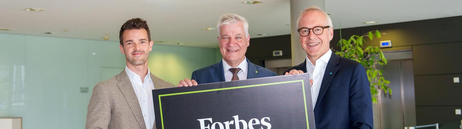 drei Männer in Anzug und Krawatte halten ein Schild mit der Aufschrift "Forbes World's Best Banks"