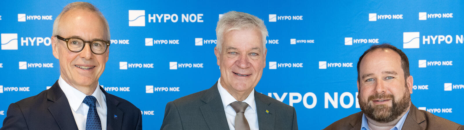 Drei Männer in Anzug und Krawatte präsentieren Ziegelsteine.