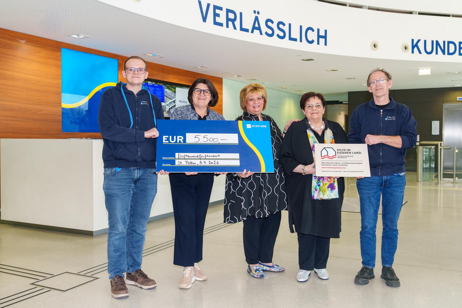Zwei Männer und drei Frauen halten zwei Schilder: Einen Spendenscheck in blau mit 5.500 Euro und ein Schild mit Vereinslogo von Hilfe im eigenen Land.