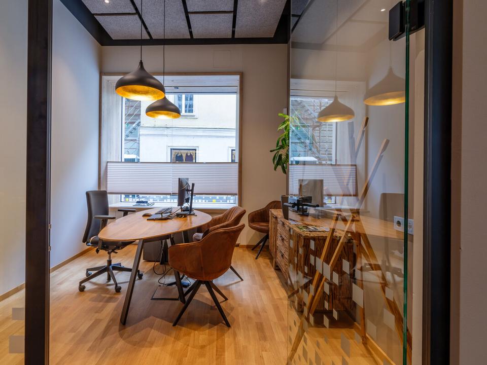 Blick von der Bürotür auf einen Schreibtisch mit Bildschirm, im Hintergrund ist ein Fenster zu sehen.
