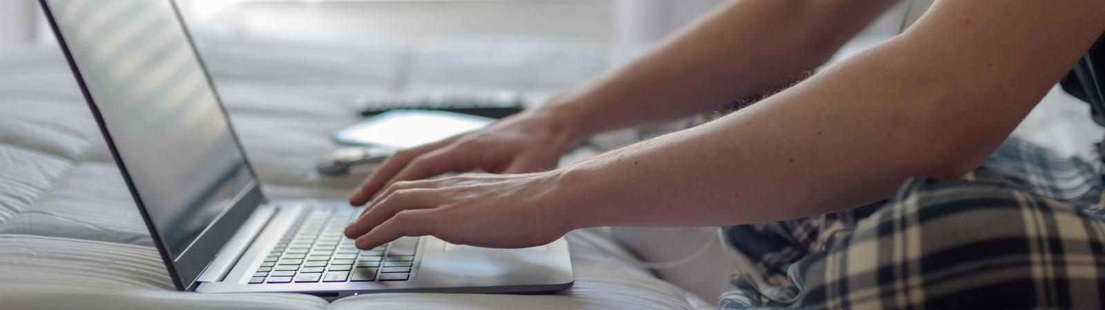 Ein junger Mann im Pyjama nutzt auf der Couch sein HYPO NOE 24/7 Internetbanking