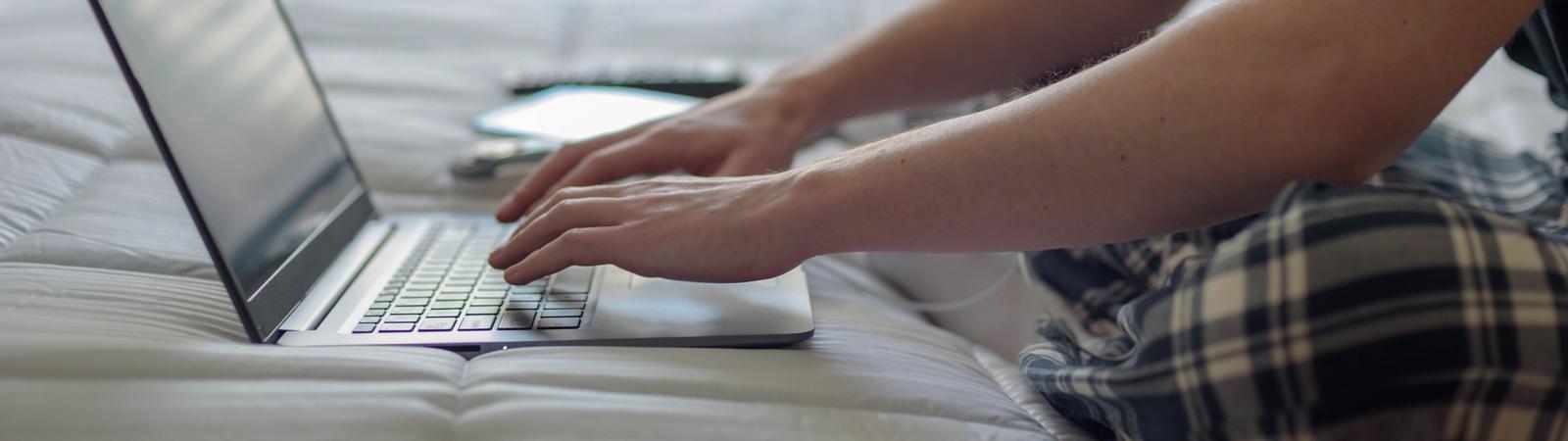 Ein junger Mann im Pyjama nutzt auf der Couch sein HYPO NOE 24/7 Internetbanking