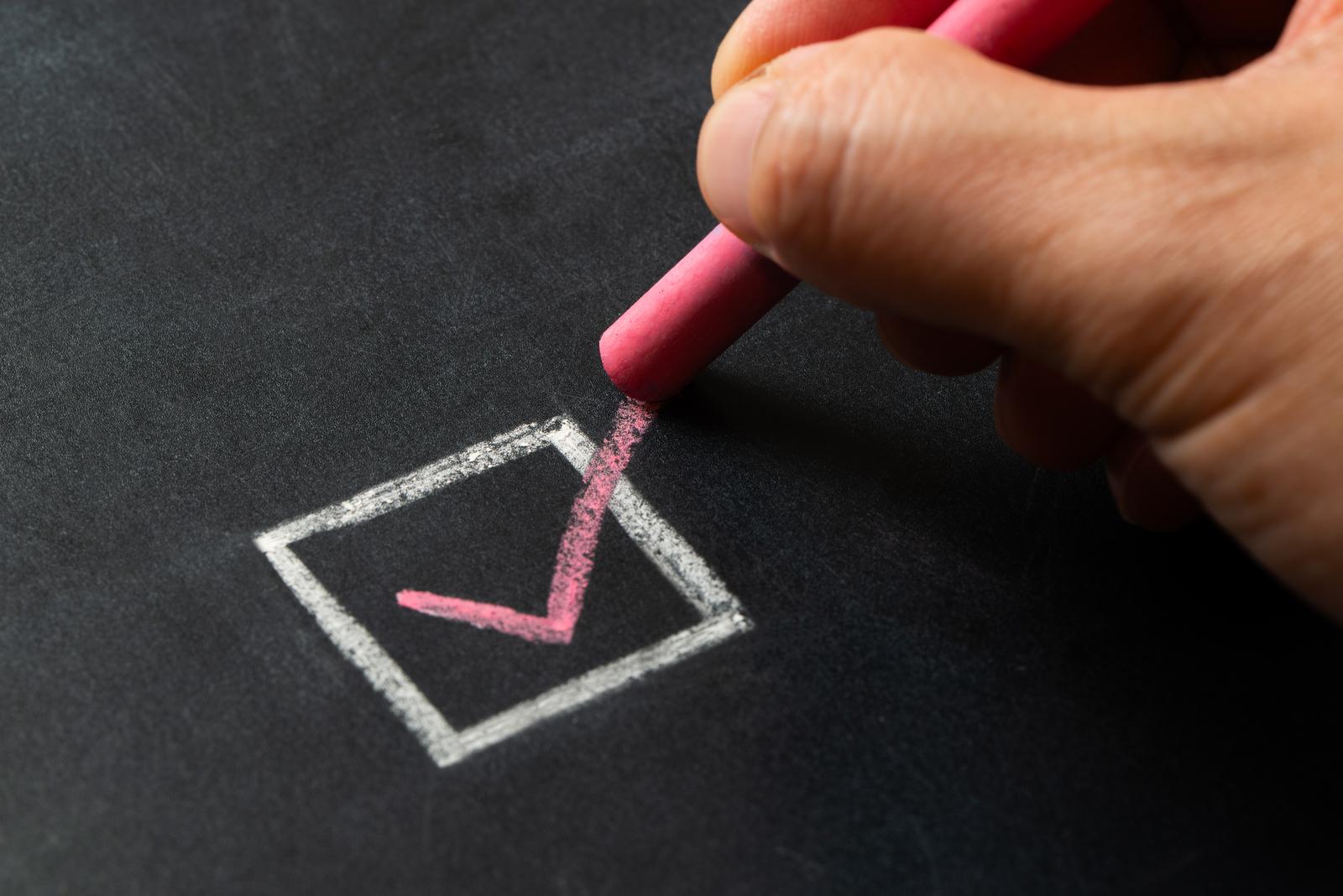 Hand mit rosa Stift malt Häkchen in das Kästchen der Checkliste