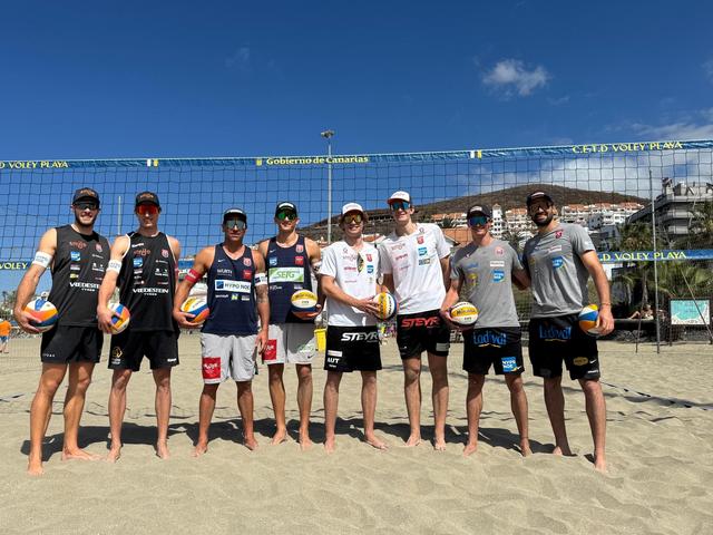 8 Beachvolleyball-Spieler stehen auf Sand vor einem Netz