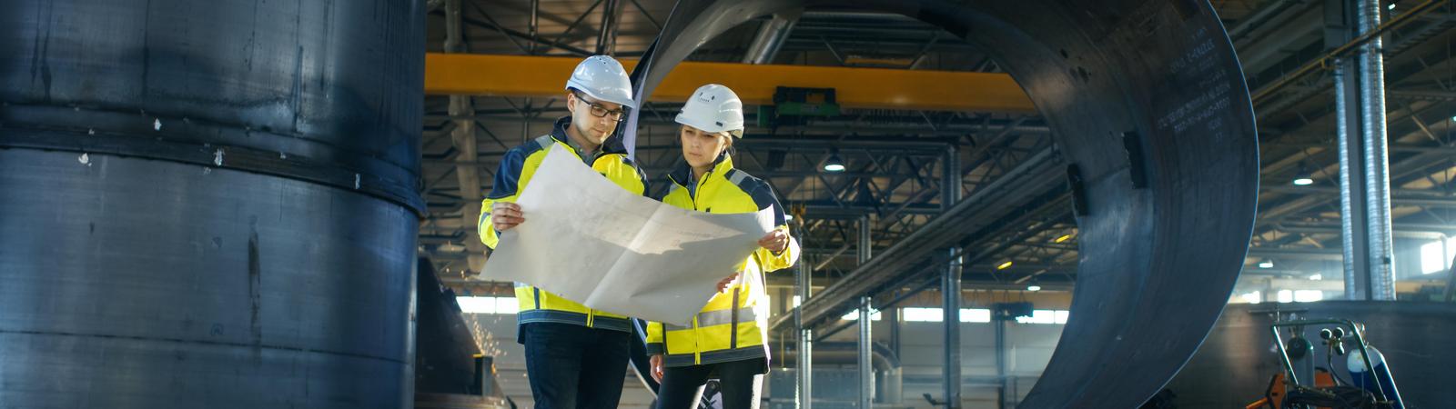 Ingenieure betrachten einen Plan, während sie in der Mitte einer Fabrik stehen