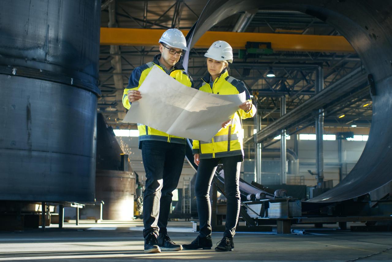 Ingenieure betrachten einen Plan, während sie in der Mitte einer Fabrik stehen