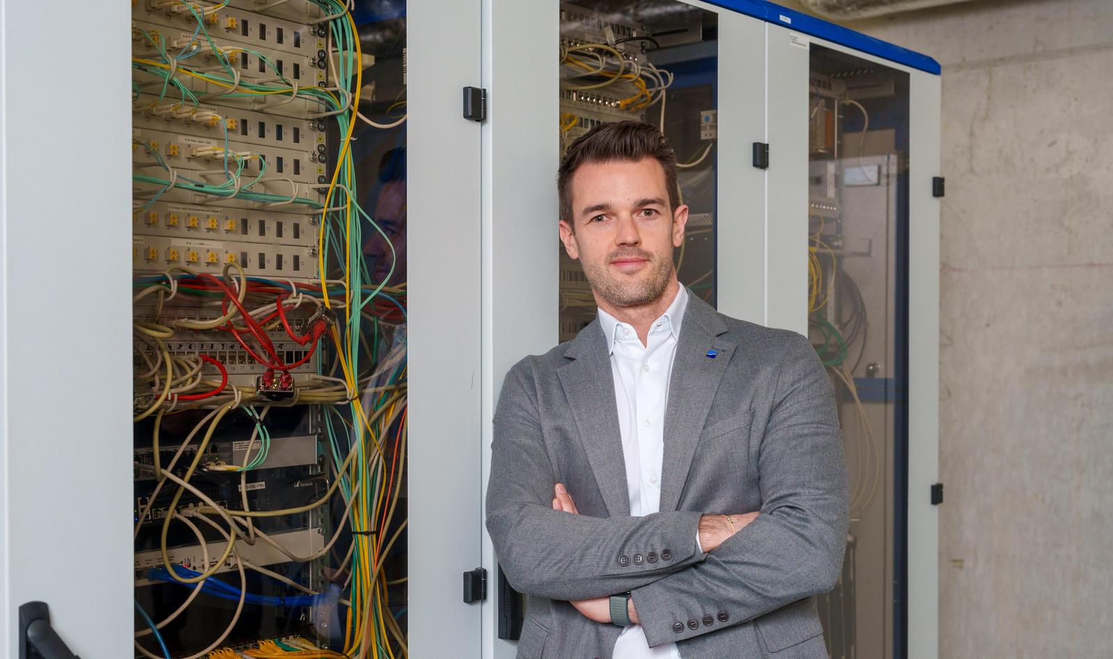 Mann mittleren Alters mit weißem Hemd und grauem Anzug lehnt an einem Serverschrank.