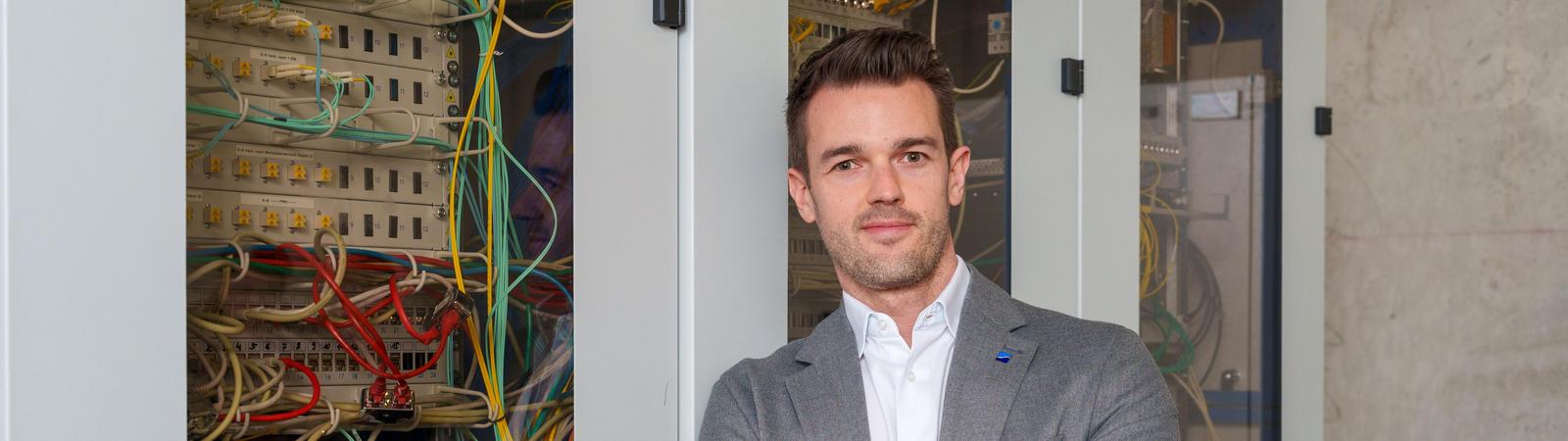 Mann mittleren Alters mit weißem Hemd und grauem Anzug lehnt an einem Serverschrank.