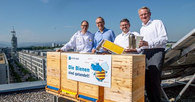 Unternehmensvertreter und Imker hinter den Bienenstöcken am Dach der HYPO NOE.