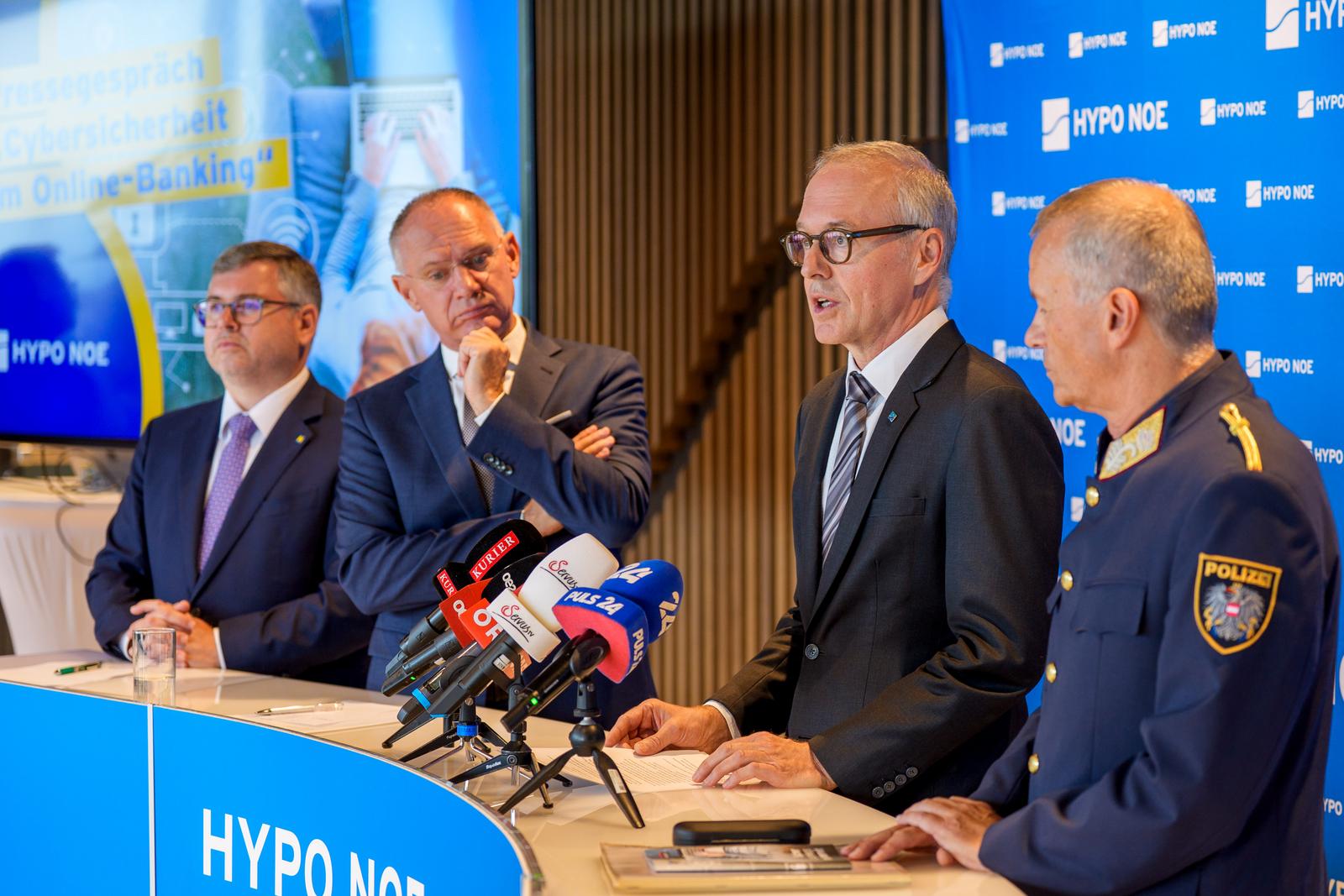 Vier Männer im Anzug stehen hinter einem Rednerpult. Ein Mann spricht und die anderen hören zu.