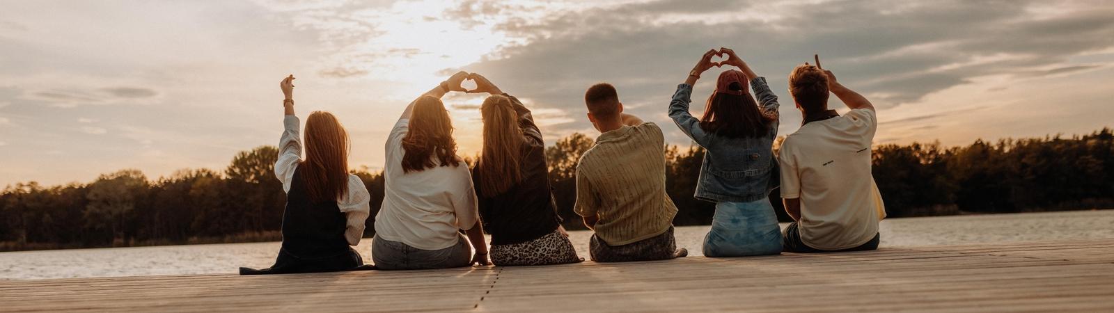 Jugendliche sitzen am Steg und betrachten den Sonnenuntergang