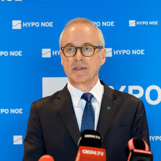 Pressekonferenz Immobilienbarometer 2026 Ein Mann in Anzug und Krawatte spricht in Mikrofone vor einem blauen Hintergrund.