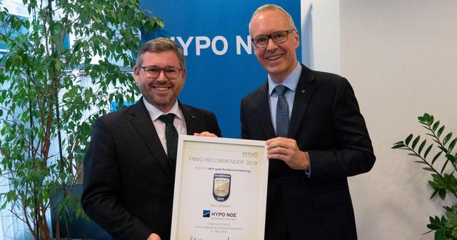 Zwei Männer mittleren Alters in Anzug und Krawatte halten eine Urkunde mit der Aufschrift "FMVÖ-Recommender: Award für sehr gute Kundenorientierung"