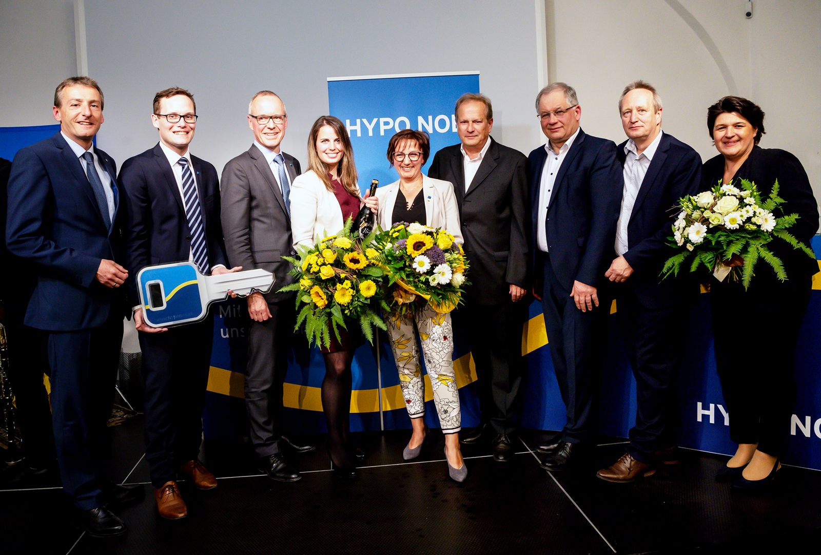 Eine Gruppe von Menschen in Business Kleidung in einem Raum bei der Schlüsselübergabe in der HYPO NOE Filiale Horn