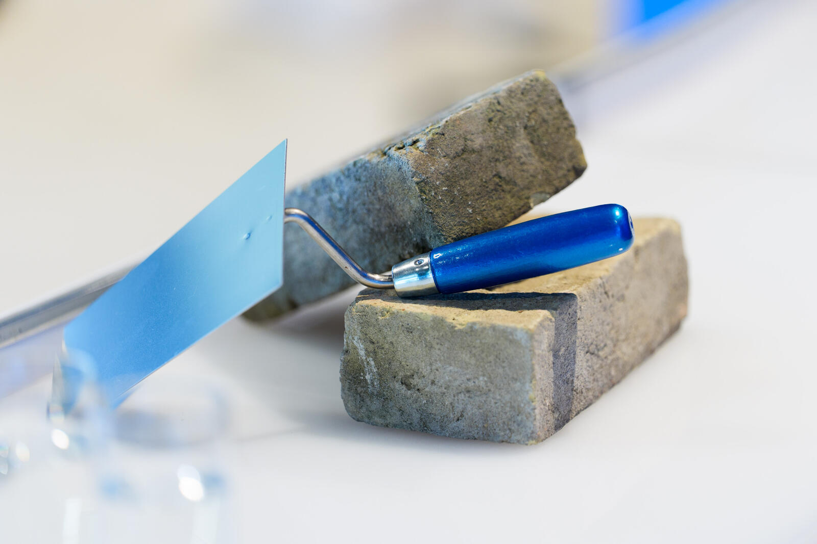 Maurerkelle mit blauem Griff liegt auf zwei Ziegelsteinen.