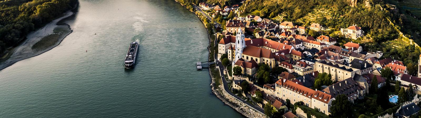Blick über den Fluss Donau mit Boot und das Tal Wachau mit dem Dorf Dürnstein im Vordergrund