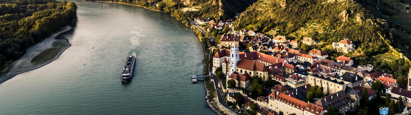 Blick über den Fluss Donau mit Boot und das Tal Wachau mit dem Dorf Dürnstein im Vordergrund