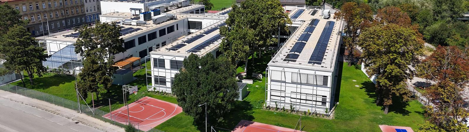 Lufansicht von zwei länglichen weißen Gebäuden mit Sport- und Grünflächen im Vordergrund