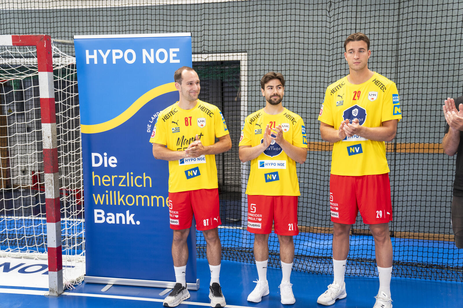 Drei Handballspieler in Vereinsdress vor HYPO NOE Banner in der Sporthalle.
