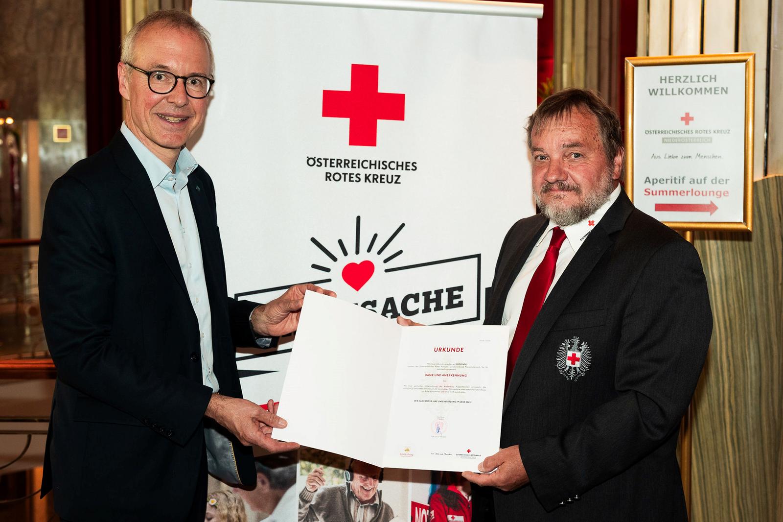 Zwei Männer in Anzug und Krawatte halten eine Urkunde.
