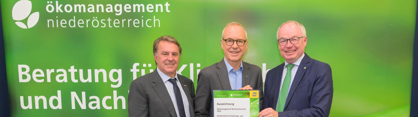 drei Männer in Anzug und Krawatte halten eine Urkunde und stehen vor einer grünen Wand