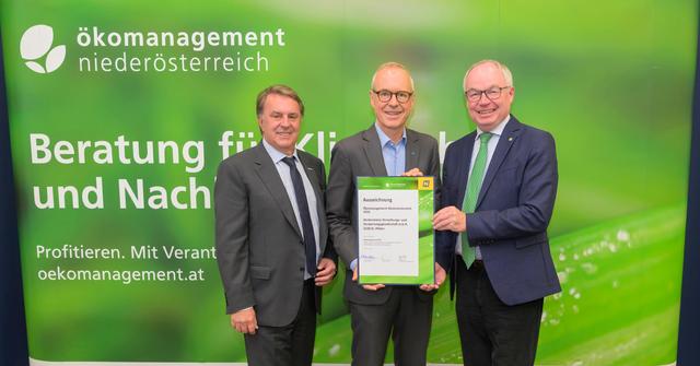 drei Männer in Anzug und Krawatte halten eine Urkunde und stehen vor einer grünen Wand