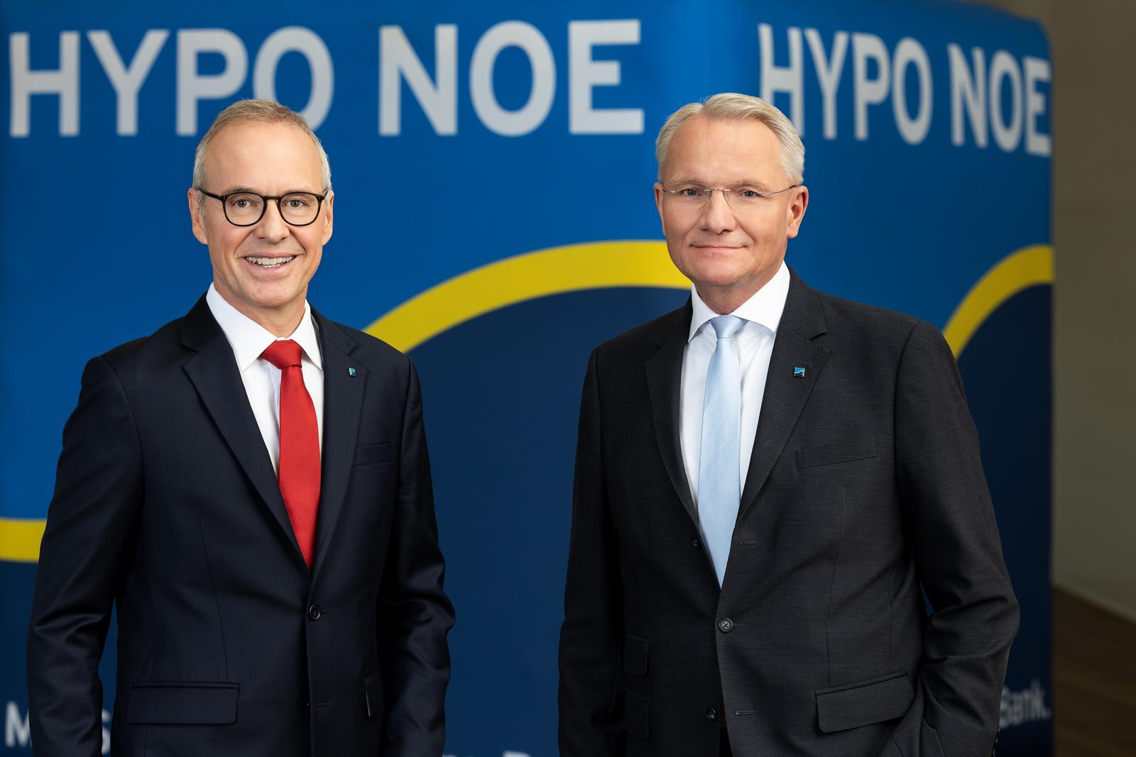 Zwei Männer mittleren Alters im Anzug stehen vor einem dunklen Hintergrund mit Aufschrift "HYPO NOE".