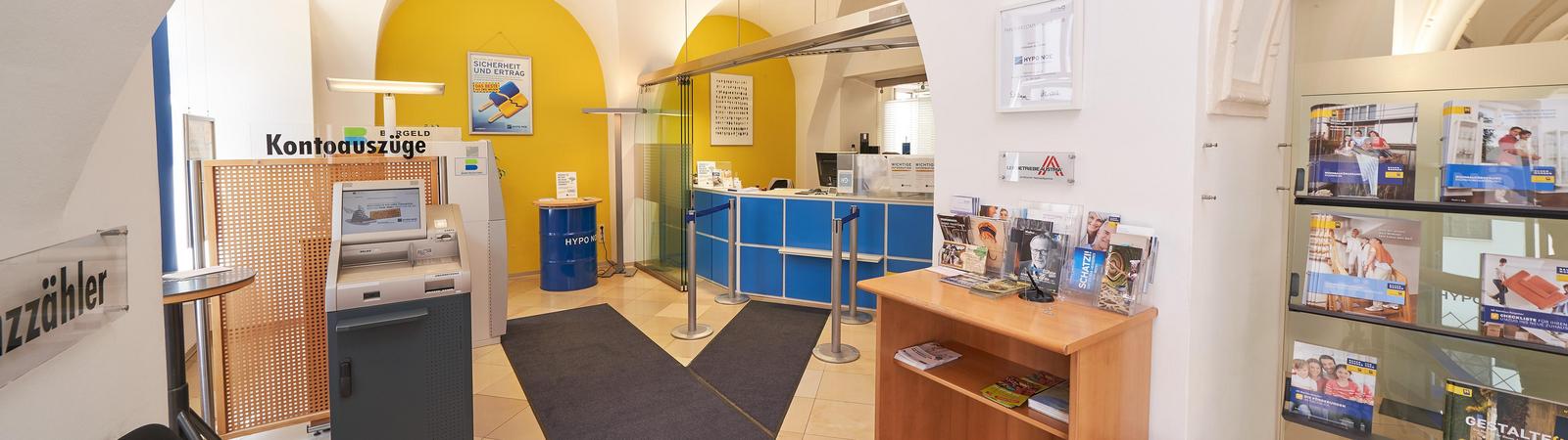 Kassenraum einer Bankfiliale: geradeaus ist ein Bankomat zu sehen, rechts ist ein Bankschalter