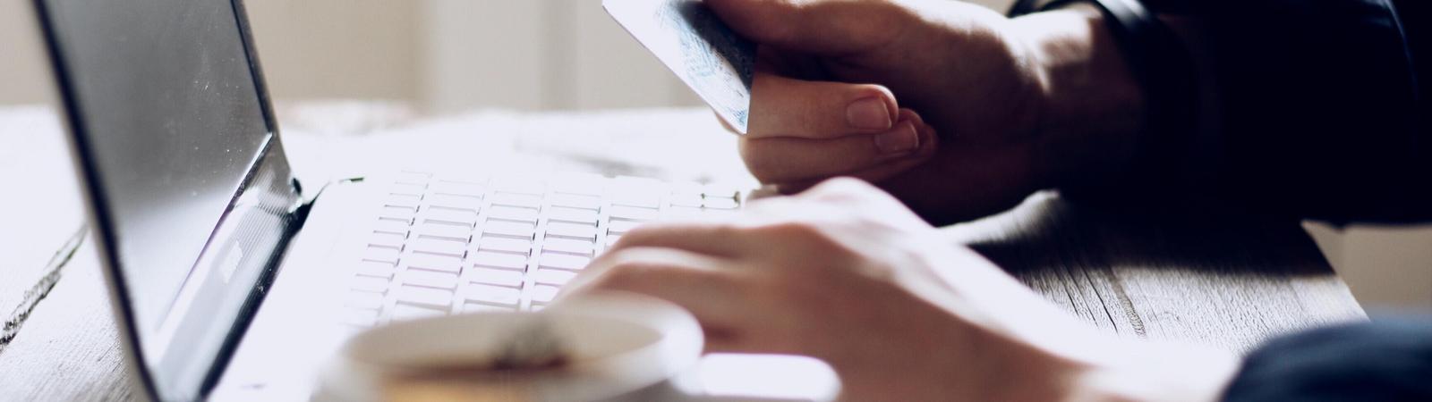 Eine Person sitzt vor einem Laptop und hält eine Kreditkarte in der Hand.