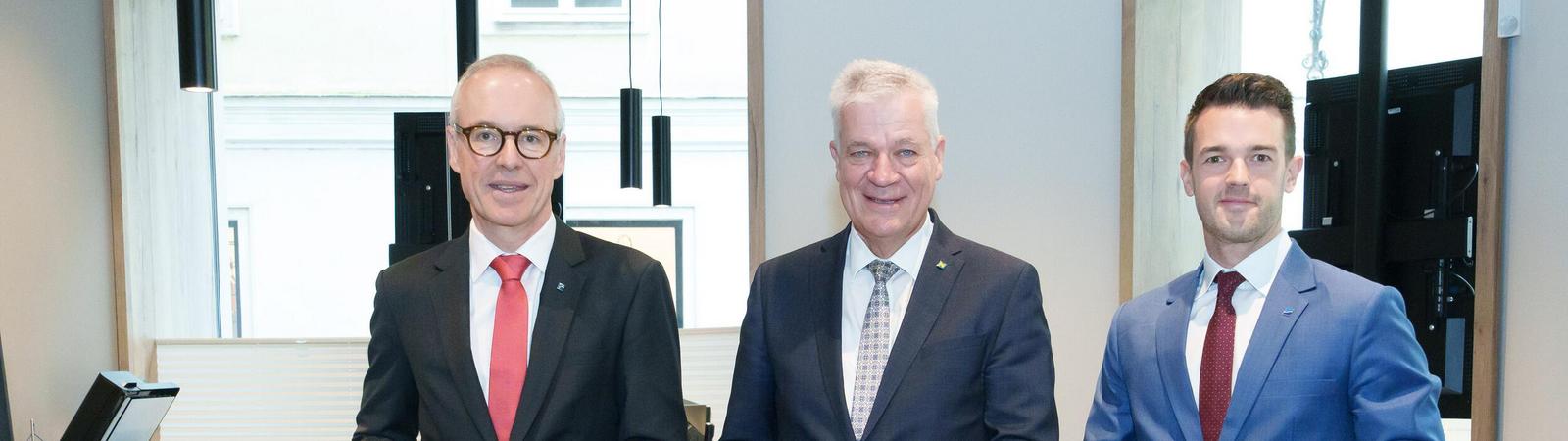 Gruppenfoto von drei Männer beim Durchschneiden eines blau-gelben Bandes.