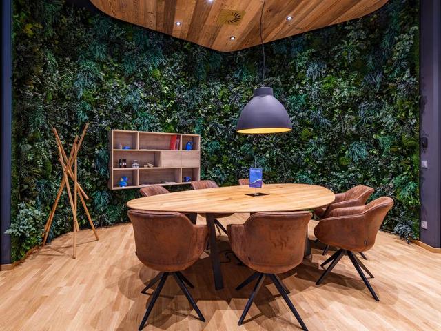 Besprechungstisch mit Sesseln in der Mitte des Raumes, an der runden begrünten Wand im Hintergrund steht ein Holzregal.