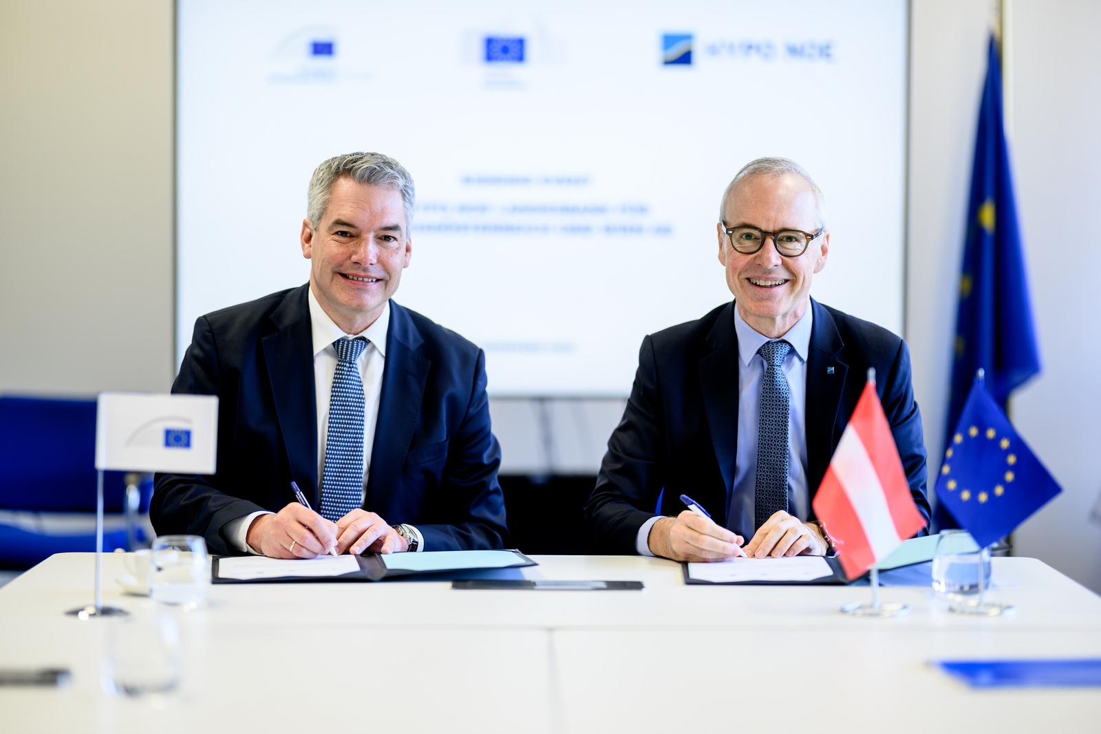 Zwei Männer in Anzug und Krawatte sitzen an einem Tisch und halten Kugelschreiber in der Hand.