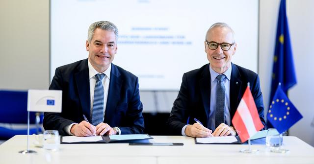 Zwei Männer in Anzug und Krawatte sitzen an einem Tisch und halten Kugelschreiber in der Hand.