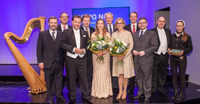 Eine Gruppe von Personen in Abendkleidung stehen auf einer Bühne vor einer Konzertharfe