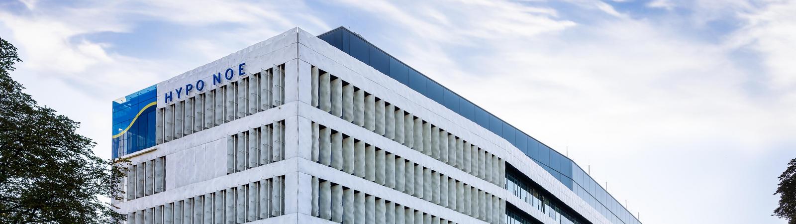 Ein weißes mehrstöckiges Bürogebäude mit Grünfläche und Bäumen davor: HYPO NOE Zentrale in Sankt Pölten