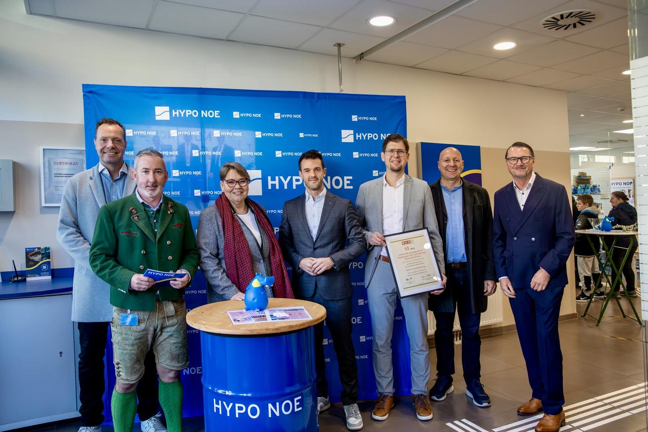 Eine Gruppe von 6 Männern und einer Frau steht vor einer blauen Wand mit Aufschrift "HYPO NOE".