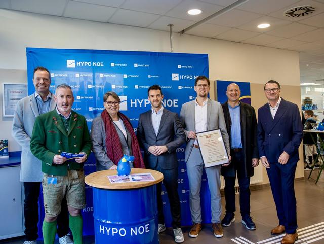 Eine Gruppe von 6 Männern und einer Frau steht vor einer blauen Wand mit Aufschrift "HYPO NOE".