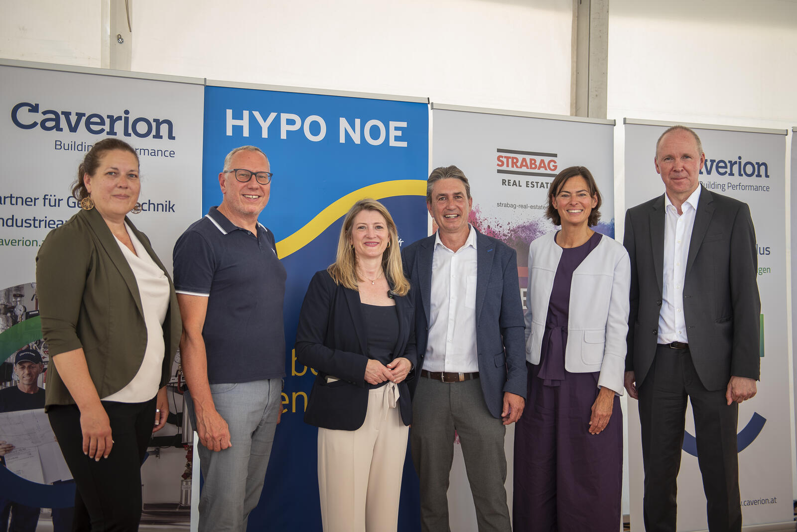 Sechs Menschen in Business Outfit stehen vor einer Wand aus Roll-ups verschiedener Unternehmen.