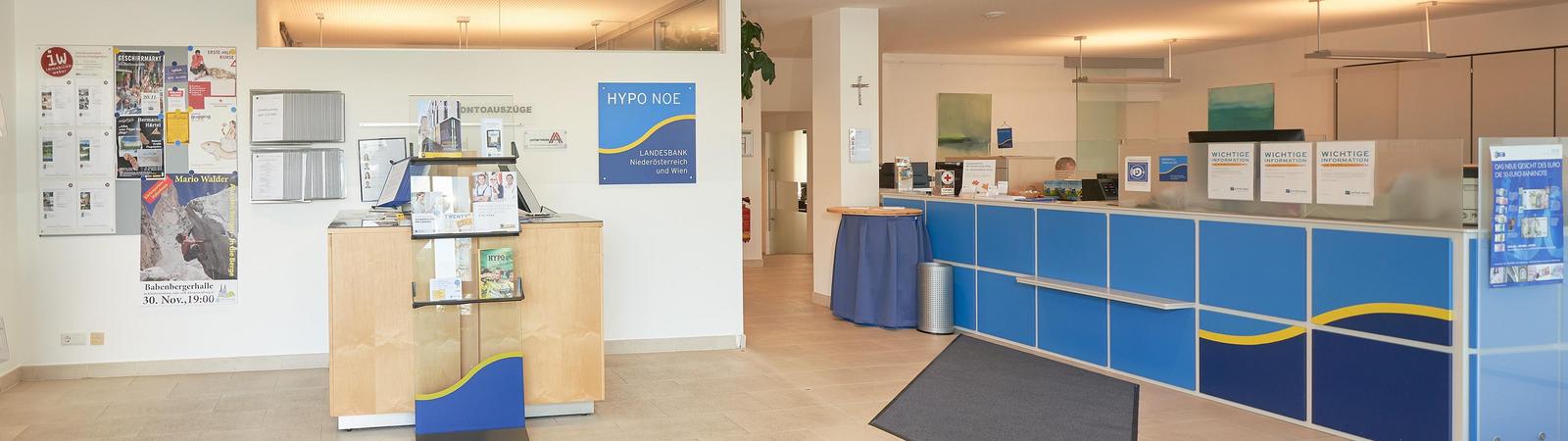 Innenraum einer Bankfiliale mit geradeaus ein paar Bankgeräten und rechterhand einem Bankschalter.