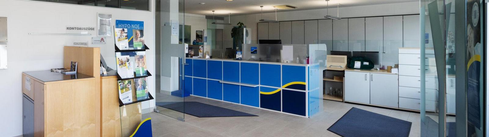 Innenraum einer Bankfiliale mit geradeaus ein paar Bankgeräten und rechterhand einem Bankschalter.