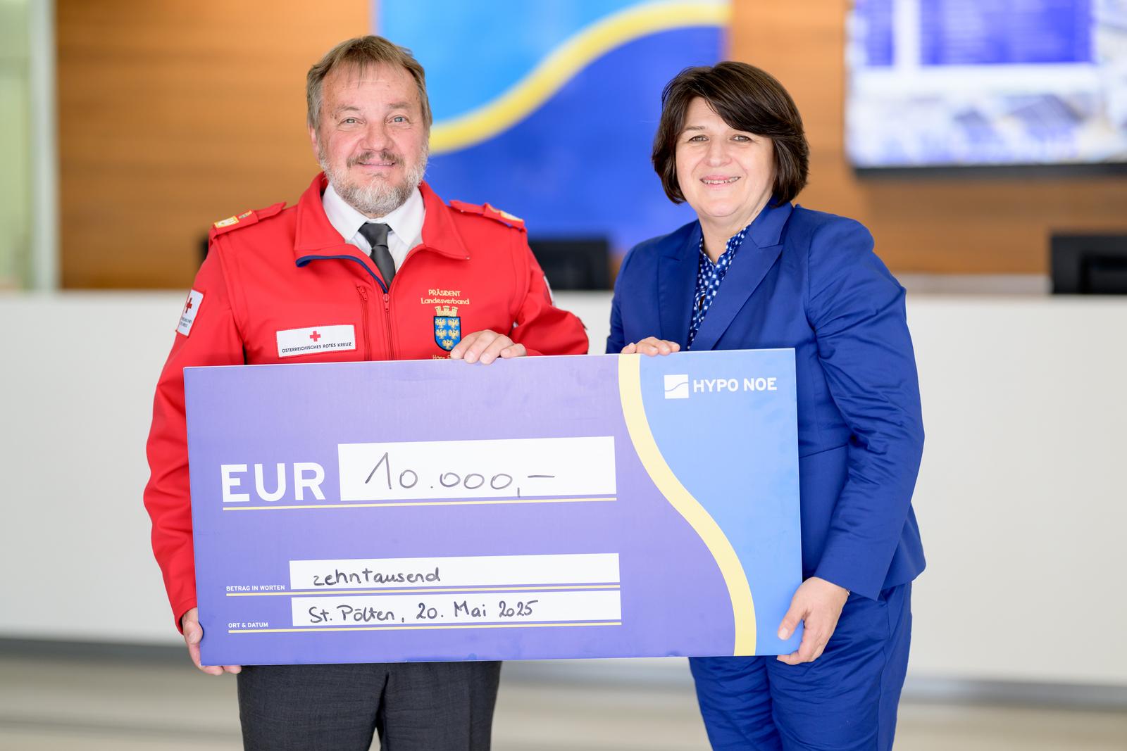 Ein älterer Mann in roter Jacke und eine Frau mittleren Alters halten einen Spendenscheck der HYPO NOE über 10.000 Euro.