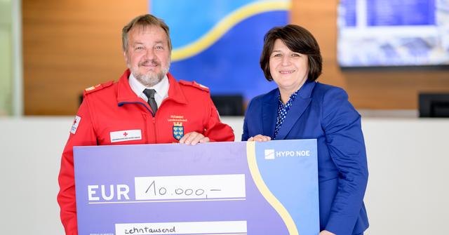 Ein älterer Mann in roter Jacke und eine Frau mittleren Alters halten einen Spendenscheck der HYPO NOE über 10.000 Euro.