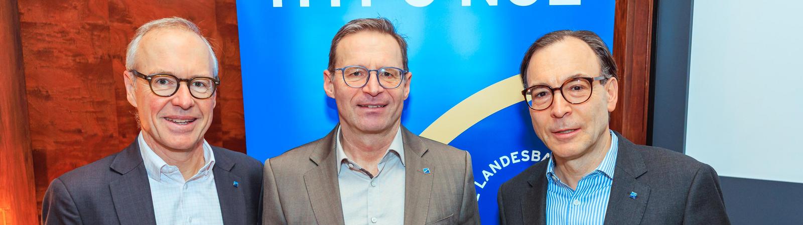 Drei Männer mittleren Alters in Anzügen stehen vor einem blauen Banner mit der Aufschrift "HYPO NOE".